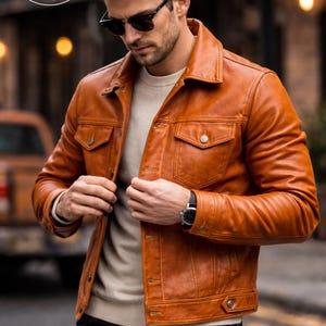 May include: A brown leather jacket with two chest pockets and two side pockets. The jacket has a button closure and a collar. The model is wearing sunglasses and a watch. The jacket is from Planio Leather.