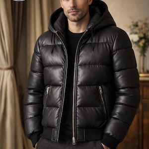 Puede incluir: Chaqueta acolchada negra con capucha y cremallera. La chaqueta tiene dobladillo y puños acanalados, y dos bolsillos con cremallera. La chaqueta está hecha de un material brillante y tiene el texto "PLANIO LEATHER" y la letra "P" en un círculo.