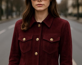 May include: A burgundy suede jacket with gold buttons and pockets. The person in the image is wearing a black hat and sunglasses. The jacket has a classic design and is suitable for various occasions.