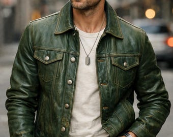 Può includere: Giacca in pelle verde con finitura invecchiata, con due tasche sul petto e chiusura con bottoni. Indossata sopra una maglietta bianca e abbinata a jeans scuri. L'immagine mostra anche un orologio argentato e una cintura in pelle marrone.