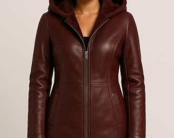 May include: A dark burgundy leather coat featuring a full-length front zipper, a hood lined with matching dark burgundy faux fur, and two vertical side pockets. The upper left chest area displays a circular logo with the text PLANIO LEATHER.