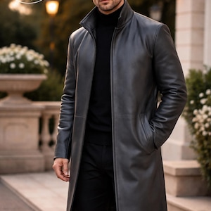May include: A charcoal gray leather coat with a high collar and long sleeves. The coat has a tailored fit and is knee-length. The model is wearing a black turtleneck and black pants. The coat is from Planio Leather.