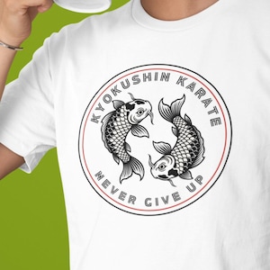 Könnte beinhalten: Weißes T-Shirt mit einem kreisförmigen Design mit zwei Koi-Fischen und den Worten "KYOKUSHIN KARATE" und "NEVER GIVE UP". Das Design ist in Schwarz und Rot gehalten. Die Person hält einen weißen Becher.