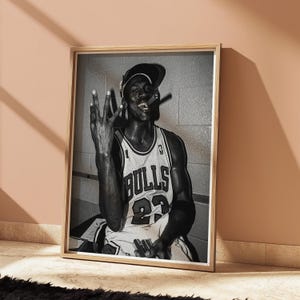 以下が含まれることがあります： シカゴ・ブルズのジャージを着たバスケットボール選手、背番号23の白黒フレームプリント。選手は葉巻を持ち、手のジェスチャーをしています。画像は木製のフレームに入っています。