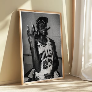 以下が含まれることがあります： シカゴ・ブルズのジャージを着たバスケットボール選手の写真、番号23。選手は3本の指を立て、葉巻を吸っています。写真は壁に立てかけられています。白黒の額入り写真。