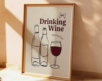 May include: A framed print with the words "Drinking Wine Feeling Fine" in burgundy lettering. The image features line drawings of two wine bottles and a wine glass filled with red wine. The frame is a light brown color.