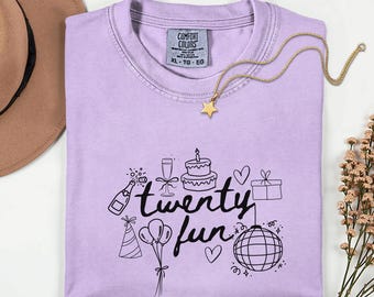 Puede incluir: Una camiseta lila con las palabras "twenty fun" y gráficos de celebración. Un collar con colgante de estrella dorada descansa sobre la camiseta. La camiseta tiene una etiqueta Comfort Colors, talla XL-TG-EG.