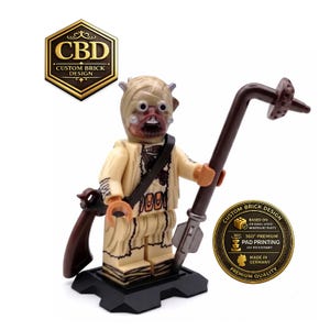 Könnte beinhalten: Eine beigefarbene Minifigur mit umwickeltem Kopf, dunkelbraunem Mundbereich und weißen Zähnen. Die Figur trägt strukturierte beigefarbene Kleidung mit einem dunkelbraunen Schulterriemen und hält eine lange braune Gaffi-Stabwaffe. Auf schwarzem Sockel.
