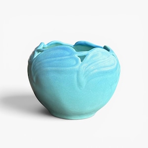 May include: A round, light blue ceramic bowl featuring a matte finish and a decorative relief pattern of stylized leaves encircling the upper rim. The bowl has a wide, open top with a scalloped edge and a smooth, curved body that tapers toward the base.