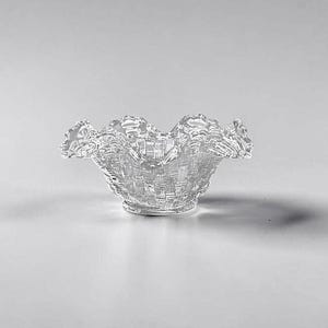 May include: A clear glass bowl with a ruffled rim. The bowl has a woven texture throughout its body and a circular base. The bowl is designed to hold small items and is suitable for decorative purposes.