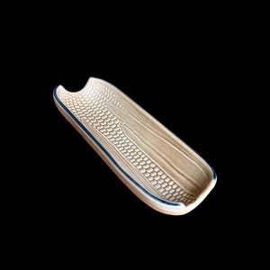 May include: A beige ceramic corn-shaped serving dish with a blue rim. The dish has a textured surface with a pattern resembling corn kernels and husks. The dish is approximately 10 inches long.