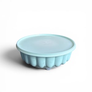 May include: A light blue, round, fluted storage container with a matching circular lid. The bowl features a scalloped exterior design with vertical ridges, providing a textured appearance. The lid is smooth and sits securely on top of the bowl.