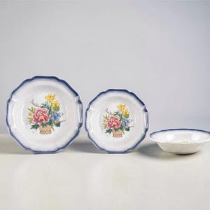 May include: A set of three ceramic dishes with a floral design. The plates and bowl have a white base with a blue scalloped edge. The floral design features pink, yellow, and blue flowers in a basket.