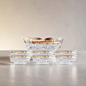 May include: A clear glass serving set consisting of one large bowl and six smaller matching bowls. Each piece features a textured, faceted geometric pattern on the exterior and a smooth, reflective gold band encircling the upper rim.