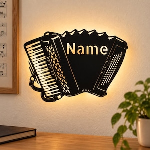May include: A black wall-mounted light fixture shaped like an accordion, featuring a cutout of the word Name on the bellows. The silhouette displays detailed keys and buttons, with a warm glow emanating from behind the metal structure.
