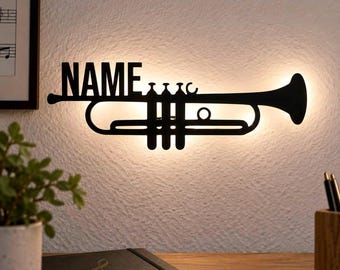 May include: A black metal wall-mounted light fixture shaped like a trumpet with the word NAME integrated into the design. The silhouette features a backlit glow that illuminates the wall behind the instrument-shaped metal cutout.