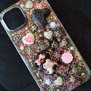 Puede incluir: Funda transparente para tel&eacute;fono decorada con purpurina, corazones, estrellas y dise&ntilde;os florales. La funda presenta un dije negro en forma de coraz&oacute;n con la palabra "TORUN" y un personaje de dibujos animados con un lazo rosa.