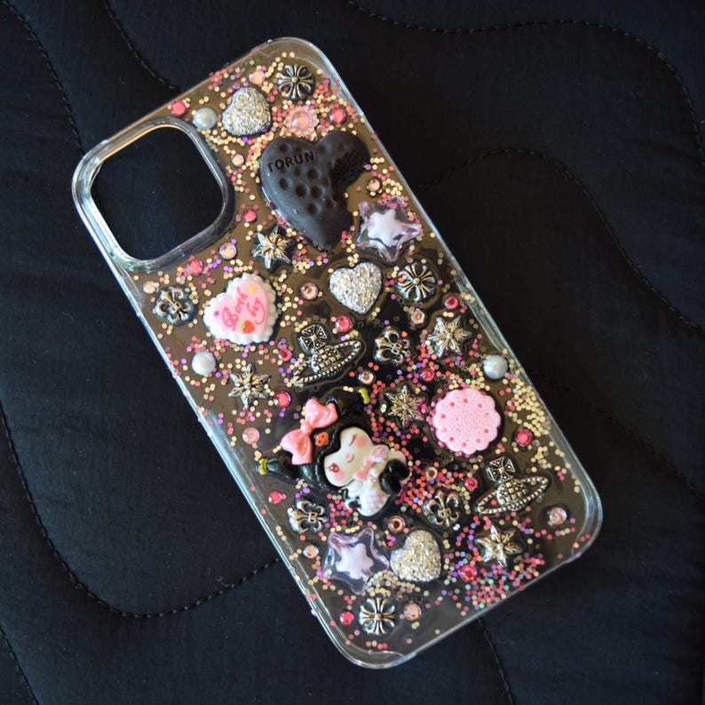 Puede incluir: Funda transparente para tel&eacute;fono decorada con purpurina, corazones, estrellas y dise&ntilde;os florales. La funda presenta un dije negro en forma de coraz&oacute;n con la palabra "TORUN" y un personaje de dibujos animados con un lazo rosa.