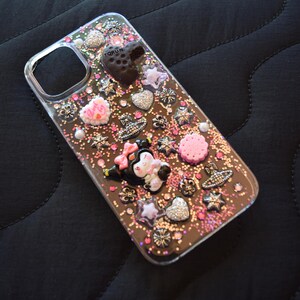Puede incluir: Funda de tel&eacute;fono transparente decorada con varios abalorios, incluyendo corazones, estrellas y una figura de Minnie Mouse. La funda tiene un fondo brillante con acentos rosas y plateados. La funda est&aacute; dise&ntilde;ada para un tel&eacute;fono.