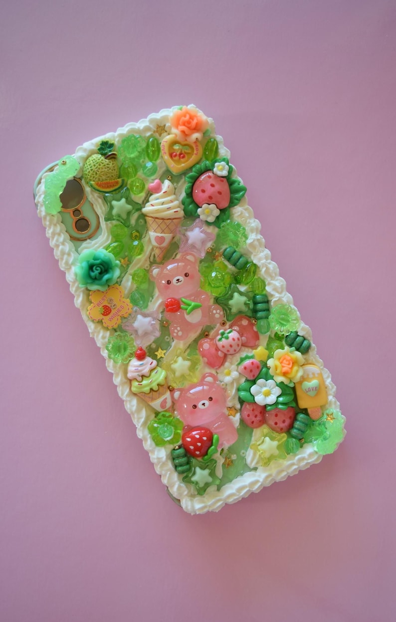 Puede incluir: Funda de tel&eacute;fono decorativa con un dise&ntilde;o caprichoso. Presenta ositos de goma rosas, fresas, conos de helado y detalles florales. Tiene un borde blanco texturizado y una combinaci&oacute;n de colores verde y blanco.