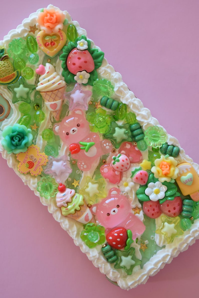 Puede incluir: Un objeto rectangular decorativo con fondo rosa, con un dise&ntilde;o caprichoso de osos rosas, fresas, conos de helado y detalles en forma de estrella. Los bordes est&aacute;n adornados con glaseado blanco.
