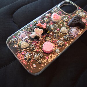 Puede incluir: Funda de tel&eacute;fono transparente decorada con adornos rosas, plateados y negros. La funda presenta una figura de Minnie Mouse, corazones, estrellas y otros elementos decorativos. La funda est&aacute; cubierta de purpurina y peque&ntilde;as cuentas rosas.
