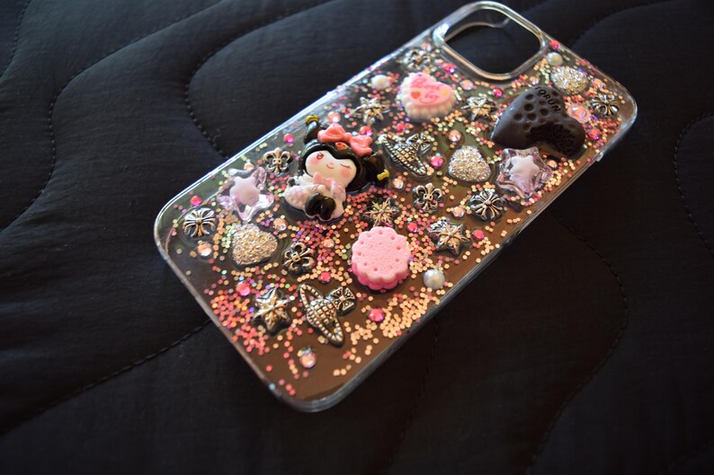 Puede incluir: Funda de tel&eacute;fono transparente decorada con adornos rosas, plateados y negros. La funda presenta una figura de Minnie Mouse, corazones, estrellas y otros elementos decorativos. La funda est&aacute; cubierta de purpurina y peque&ntilde;as cuentas rosas.