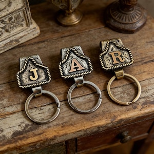 May include: Three metal keychains with the letters J, A, and R. Each keychain has a decorative top with a rope design and a circular key ring. The letters are in a contrasting gold color.