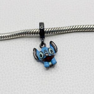 Puede incluir: Un charm de esmalte azul con el personaje Stitch de Lilo & Stitch. El charm tiene una anilla negra y est&aacute; unido a una cadena plateada. Stitch tiene orejas grandes, boca roja y cuerpo azul claro.