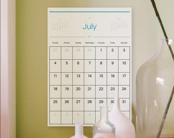 Può includere: Un calendario da parete per luglio 2021 con una griglia a linee nere su sfondo bianco. Il nome del mese July è stampato in blu al centro in alto. Piccoli calendari per giugno e agosto sono visibili negli angoli superiori.