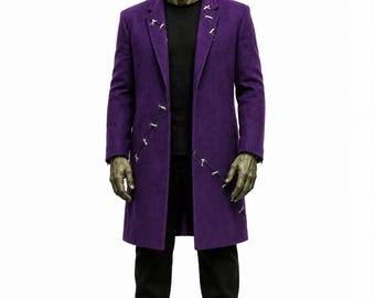May include: A figure with green skin and a flat-top hairstyle wearing a long purple coat with silver-colored metal stitch-like accents along the lapels and front, a black t-shirt, black trousers, and black platform boots against a white background.