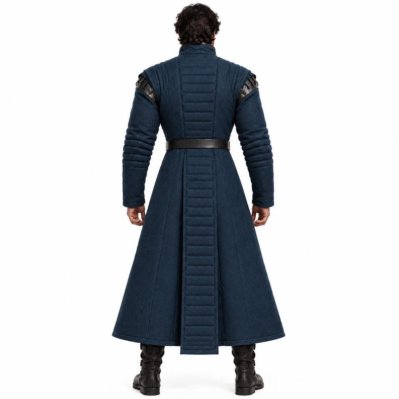 May include: A long, dark blue coat featuring a high collar, quilted vertical paneling on the back and sleeves, and a dark brown belt at the waist. The garment has structured shoulders with dark leather-like accents and reaches the mid-calf.