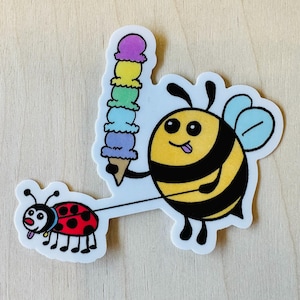 Könnte beinhalten: Eine Cartoon-Biene mit einem gelbschwarzen gestreiften Körper und einem blauen Flügel, die ein Regenbogen-Eis am Stiel hält und eine rote Marienkäfer mit schwarzen Punkten an der Leine spazieren führt.