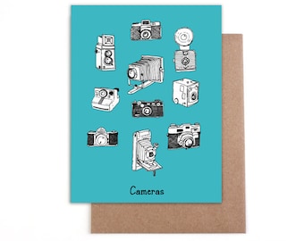 Pode incluir: Um cartão azul turquesa com uma ilustração em preto e branco de várias câmeras. O texto "Cameras" está impresso na parte inferior do cartão.