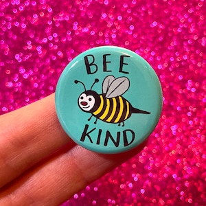 May include: A turquoise blue button with a cartoon bee and the text "BEE KIND" in black lettering.