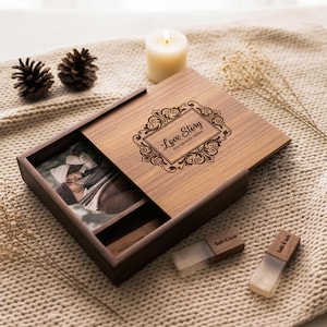 May include: A wooden keepsake box with a sliding lid, engraved with the words "Love Story" in an ornate frame. Inside, a photograph and USB drives are visible. The box is open, revealing its contents, and sits on a textured surface.
