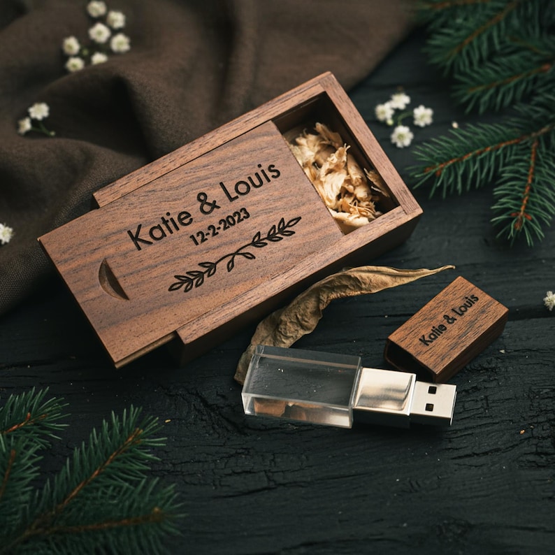 May include: A wooden USB flash drive and matching box with the names "Katie & Louis" and the date "12-2-2023" engraved on them. The box is open, revealing dried filler. The USB drive has a clear plastic casing.