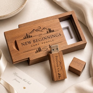 May include: A rectangular wooden USB flash drive with a matching sliding lid box. The box is engraved with a mountain landscape and the text NEW BEGINNINGS SAME PEOPLE. The USB drive is engraved with Forever Us and a mountain graphic.
