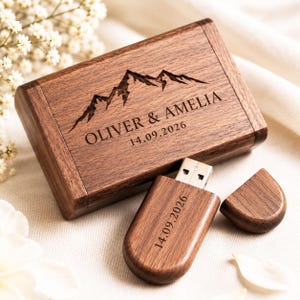 Può includere: Una scatola rettangolare in legno e una chiavetta USB in legno abbinata con cappuccio rimovibile. Il coperchio della scatola presenta un grafico di montagna inciso, i nomi OLIVER & AMELIA e la data 14.09.2026. La chiavetta USB riporta 14.09.2026.