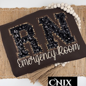 May include: Brown RN Emergency Room applique with black sequin letters and leopard print trim. The design includes the text "Emergency Room" in a cursive font. The image also features a CNIX designs logo.