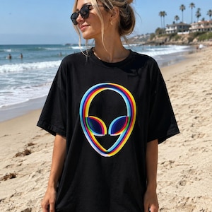 May include: A black short-sleeved t-shirt featuring a large, centered graphic of an alien head. The alien head design is composed of concentric, vibrant rainbow-colored rings in shades of red, orange, yellow, green, blue, and purple.