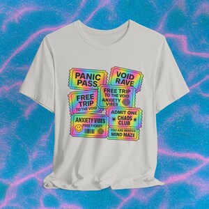 Könnte beinhalten: Weißes T-Shirt mit einem farbenfrohen Aufdruck von gefälschten Tickets mit Sätzen wie "Panic Pass", "Void Rave" und "Anxiety Vibes". Das Design hat regenbogenfarbene Ränder und Text und erzeugt eine lebendige Ästhetik. Das Shirt wird auf einem wellenförmigen blauen Hintergrund präsentiert.
