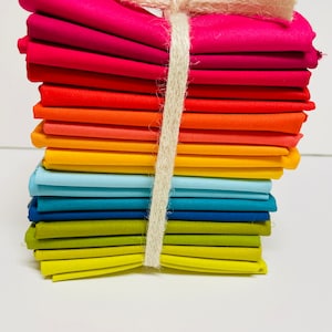 May include: A stack of colorful fabric squares tied together with twine. The fabric is arranged in a rainbow pattern, starting with pink and ending with yellow.