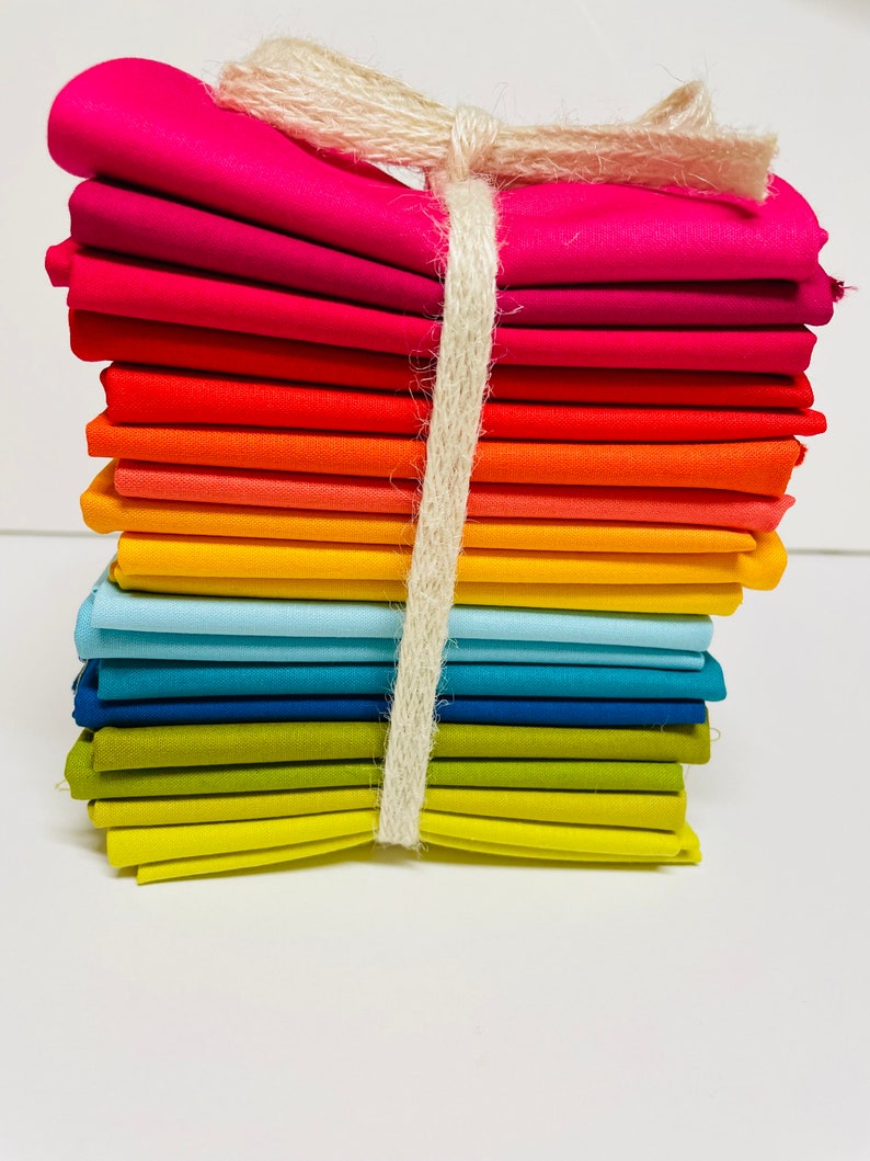 May include: A stack of colorful fabric squares tied together with twine. The fabric is arranged in a rainbow pattern, starting with pink and ending with yellow.
