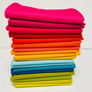 May include: A stack of 15 fabric squares in a rainbow color gradient, starting with pink and ending with yellow. The fabric is smooth and has a slight sheen.