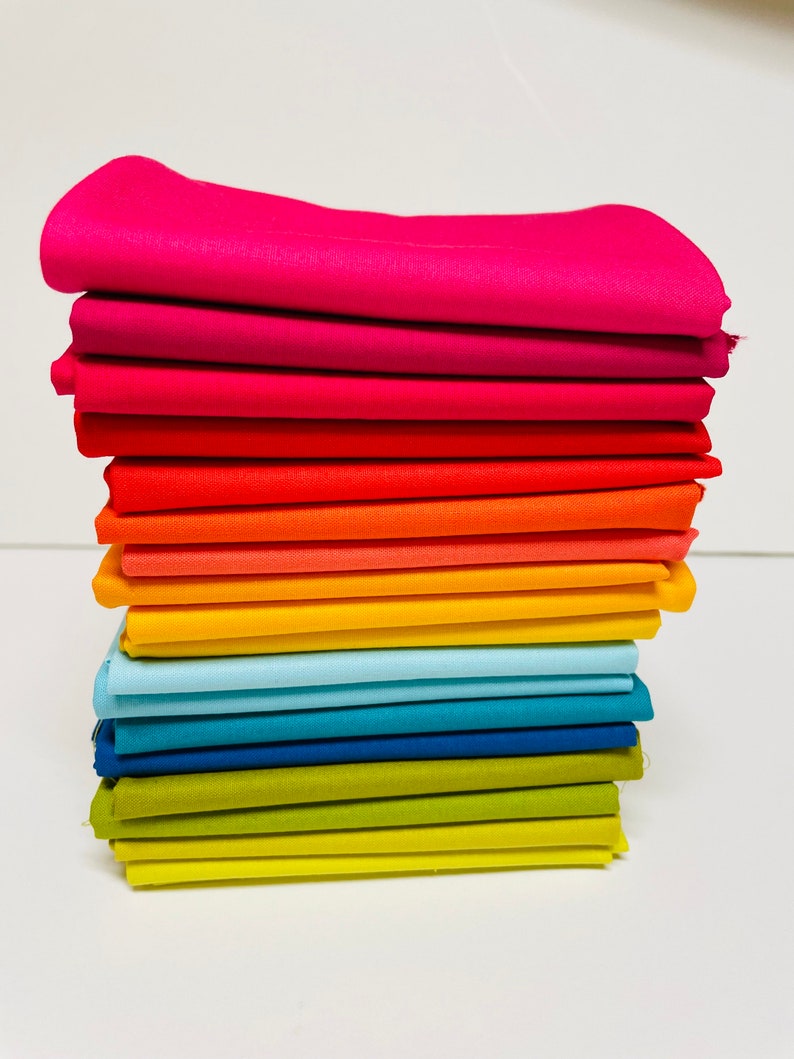 May include: A stack of 15 fabric squares in a rainbow color gradient, starting with pink and ending with yellow. The fabric is smooth and has a slight sheen.