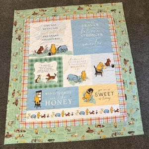 May include: A rectangular quilt featuring Winnie the Pooh characters and inspirational quotes. The design includes panels with text like 'Life was meant for good friends' and 'Kind words are like honey,' surrounded by a light green patterned border.