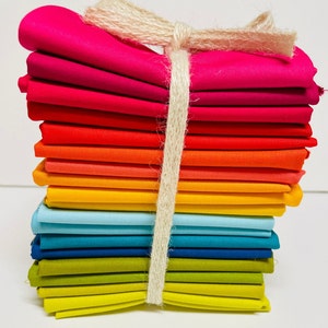 May include: A stack of 15 colorful fabric squares tied together with twine. The fabric squares are arranged in a rainbow pattern, starting with pink and ending with yellow.