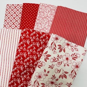 May include: A collection of red and white patterned fabrics. Designs include floral, striped, and geometric patterns. The fabrics are folded and arranged to display the variety of designs and textures.