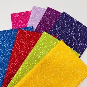 May include: A collection of colorful fabric squares, each displaying a speckled pattern of white dots. The fabrics are arranged in a fan shape, showcasing a variety of hues including pink, purple, blue, red, green, and yellow. Ideal for quilting and crafting projects.